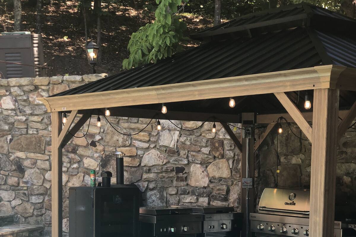 An outdoor barbecue area with a stone wall backdrop, a covered grill station, and a poolside setting.