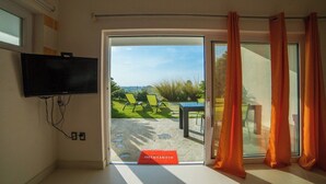Een kamer met een aan de muur bevestigde televisie, een glazen schuifdeur die leidt naar een buitenruimte met een zwembad en stoelen, en een rode mat op de vloer.
