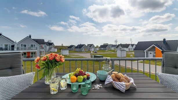 A wooden deck with a table set for a meal, featuring a fruit plate, a vase of flowers, and a basket of bread. - Modern apartment with sea view, sauna and large balcony (Kappeln)