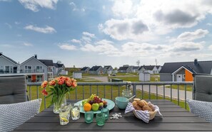 A wooden deck with a table set for a meal, featuring a fruit plate, a vase of flowers, and a basket of bread. - Modern apartment with a view of the sea, a sauna, and a large balcony (Kappeln)