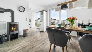 A modern kitchen with a wood-burning stove, large windows, and a dining area with a table set for two. - Modern apartment with sea view, sauna and large balcony (Kappeln)