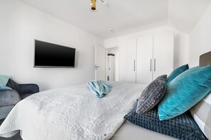 A modern bedroom with a large bed, a flat-screen TV mounted on the wall, and a wardrobe with sliding doors. - Modern apartment with sea view, sauna and large balcony (Kappeln)
