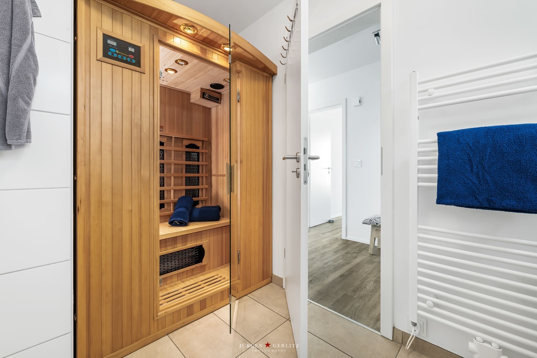 A wooden sauna with a glass door, a blue towel hanging on the wall, and a white radiator.