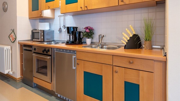 Una cucina con mobili in legno, un forno a microonde, una moka, un lavello e una lavastoviglie.