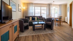 A modern living room with a sofa set, a coffee table, a TV, and a dining area with chairs and a table. - Comfort apartment with 1 bedroom and terrace on the first floor (Ostseebad Binz)