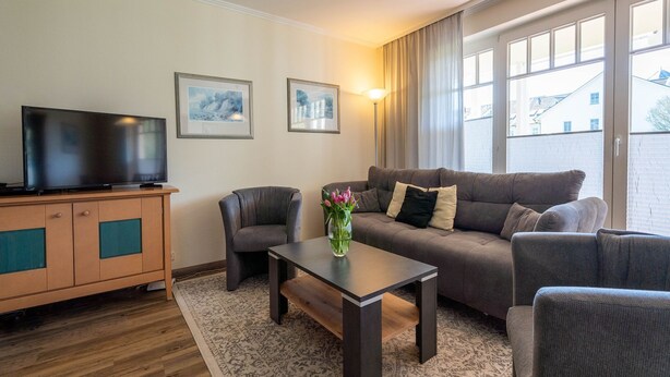 A modern living room with a sofa, armchairs, a coffee table, and a TV on a wooden cabinet. - Comfort apartment with 1 bedroom and terrace on the first floor (Ostseebad Binz)