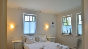 Et rent, veloplyst soveværelse med en stor seng, sengeborde og to vinduer med persienner.