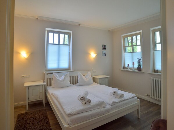 Quarto limpo e bem iluminado com uma cama grande, mesas de cabeceira e duas janelas com persianas.