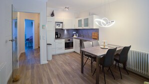 Et moderne køkken med hvide skabe, indbygget mikroovn og et spiseområde med bord og stole.