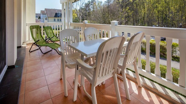 A covered patio with a table and chairs, a view of a residential area, and a white railing.