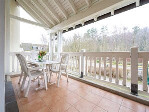 Une terrasse couverte avec une balustrade blanche, une table avec des chaises et une vue sur un quartier résidentiel.