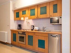 A modern kitchen with wooden cabinets, a built-in oven, a microwave, a coffee maker, and a dishwasher.