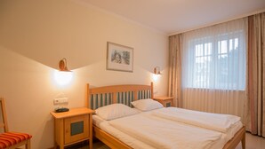 A hotel room with a double bed, two bedside tables, a chair, a painting on the wall, and a window with curtains.