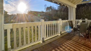 Una terrazza esterna coperta con ringhiera bianca, pavimento in legno e vista su un quartiere residenziale con case e alberi.