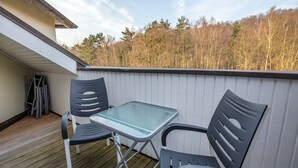En balkon med et glasbord og to stole, trægulv og gelænder i hvid.