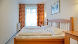 A hotel room with a wooden bed, a nightstand, a radiator, and a painting on the wall.
