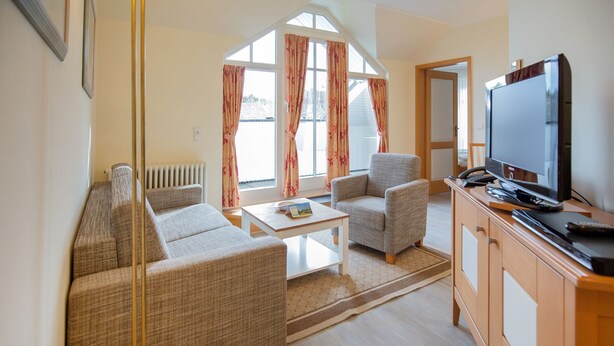 A living room with a sofa, armchairs, a coffee table, a television, and a radiator.