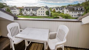 A balcony with a white table and two white chairs, overlooking a row of townhouses with a clear sky above.