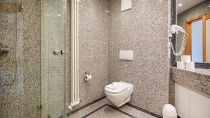 A modern bathroom with a glass shower enclosure, a white toilet, and a marble-tiled floor.