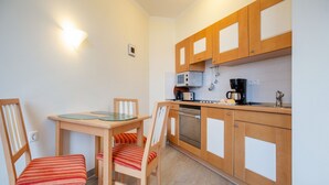 A compact kitchen with wooden cabinets, a microwave, a coffee maker, and a dishwasher. There is a dining table with chairs.