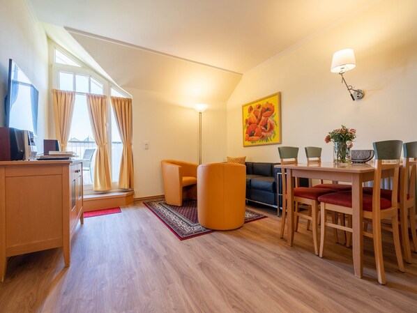 A modern living room with a wooden desk, a sofa, a dining table with chairs, and a painting on the wall.