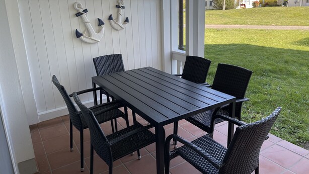 A covered patio with a table and chairs, a white fence with decorative anchors, and a view of a grassy yard and houses in the background. - Comfort apartment with 1 bedroom and terrace on the first floor (Ostseebad Binz)