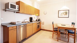A modern kitchen with wooden cabinets, stainless steel appliances, a microwave, and a dining area with a table and chairs. - Classic apartment with 1 bedroom and balcony on the upper floor (Ostseebad Binz)