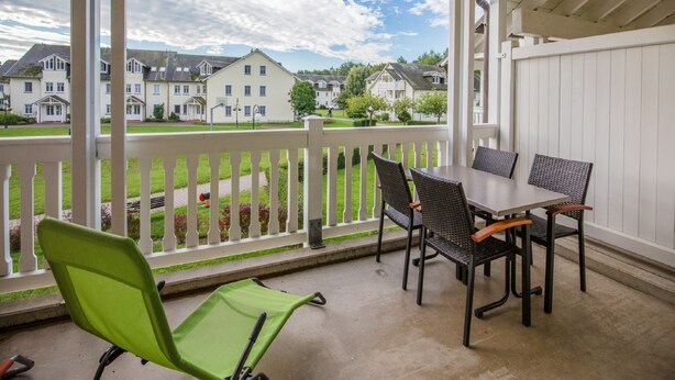 A covered outdoor area with a table and chairs, a green chair, and a view of houses in the background. - Classic apartment with 1 bedroom and balcony on the upper floor (Ostseebad Binz)