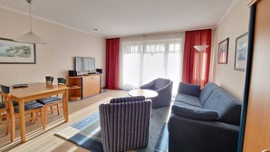 A modern living room with a wooden dining table, blue sofa, and striped ottoman. - Classic apartment with 1 bedroom and balcony on the upper floor (Ostseebad Binz)