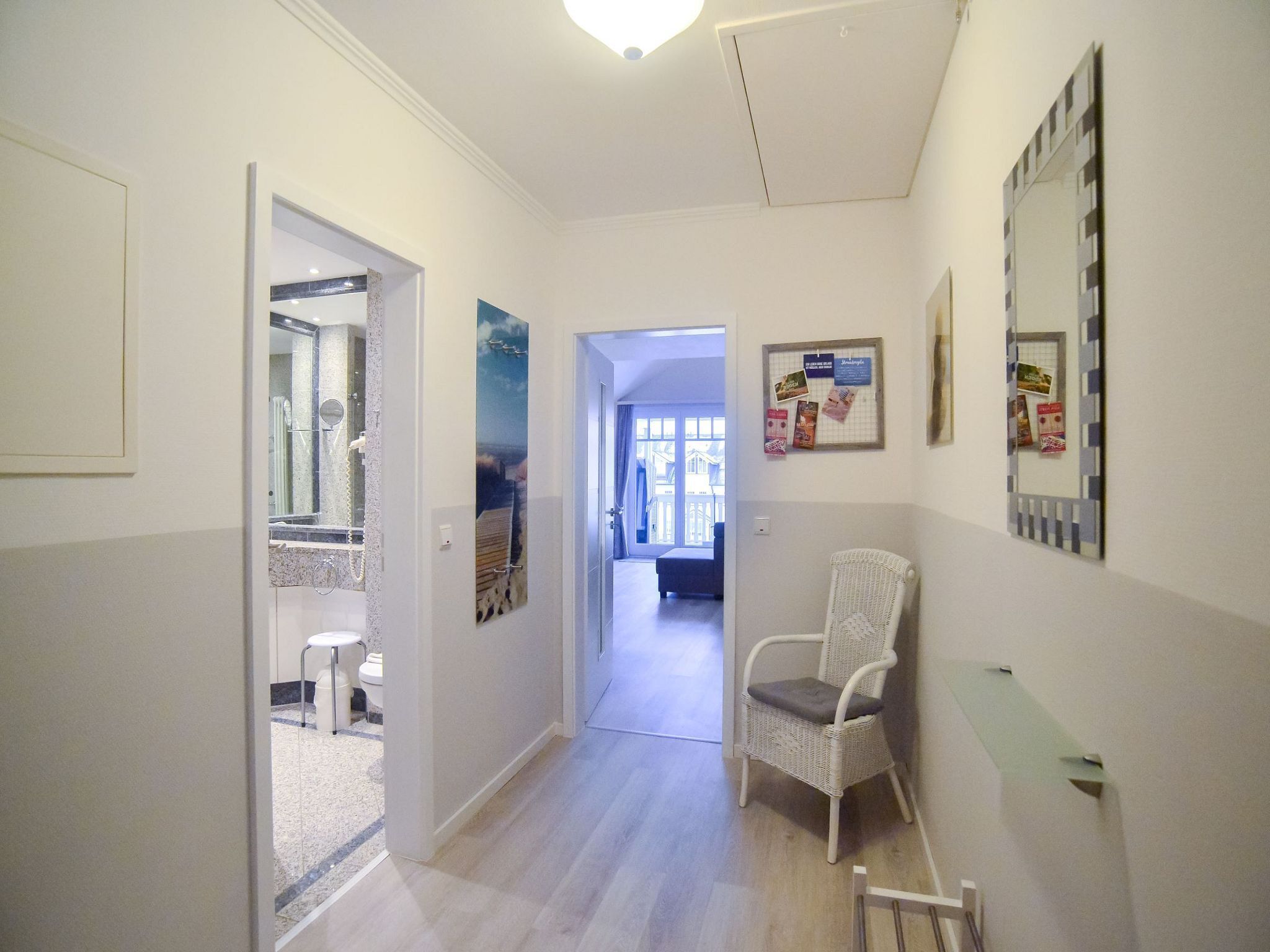 A hallway with a white chair, a wall-mounted mirror, and a bulletin board with notices.
