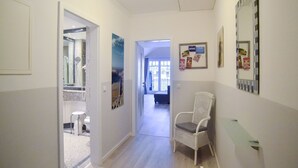 A hallway with a white chair, a wall-mounted mirror, and a bulletin board with notices. - Comfort plus apartment with 1 bedroom and balcony on the top floor (Ostseebad Binz)
