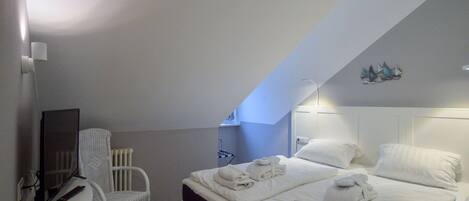 A bedroom with a bed, a desk, a chair, and a small wall-mounted shelf.