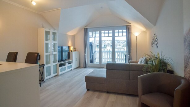 A spacious living area with a large window, a sofa, a television, and a cabinet. - Comfort plus apartment with 1 bedroom and balcony on the top floor (Ostseebad Binz)