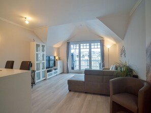 A spacious living area with a large window, a sofa, a television, and a cabinet. - Comfort Plus Apartment with 1 bedroom and a balcony on the top floor (Ostseebad Binz)