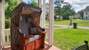 Un porche cubierto con un banco de madera y una silla de mimbre.
