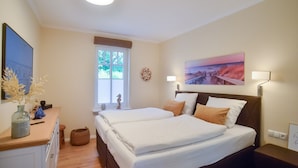 Habitación de hotel con dos camas, un aparador de madera, una ventana con persianas, una lámpara de pared y un cuadro.