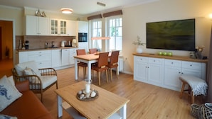 Una cocina moderna con armarios blancos, un comedor con mesa y sillas de madera, y un cuadro grande en la pared.
