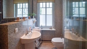 Un baño moderno con encimeras de granito, un espejo grande, un lavabo, un inodoro y una zona de ducha.
