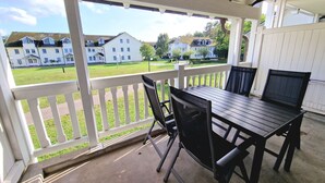 A covered patio with a table and chairs, overlooking a grassy area with houses in the background. - Komfort Ferienwohnung mit 1 Schlafzimmer und Balkon im Obergeschoss (Ostseebad Binz)
