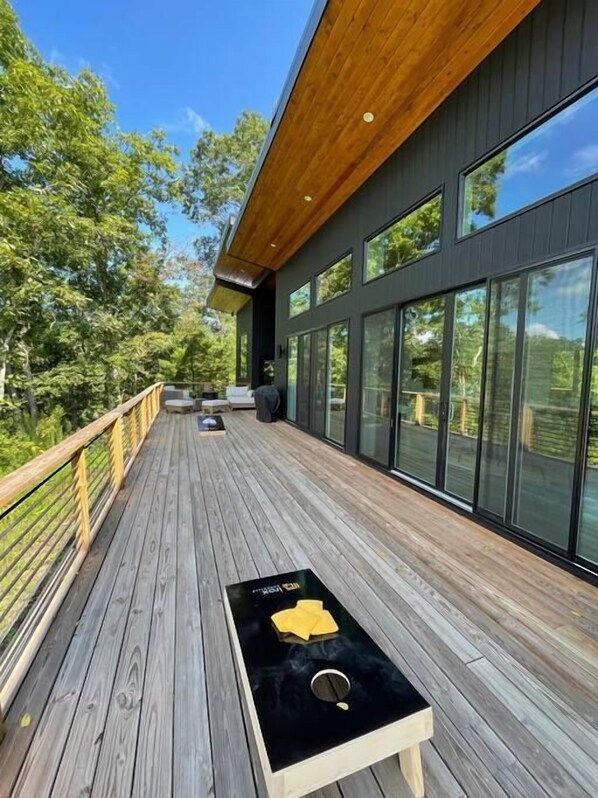 Enjoy the serene forest views from this outdoor deck, featuring a comfortable seating area and a large window-lined building.