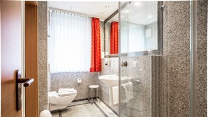 A modern bathroom with a toilet, sink, and glass shower enclosure. - Comfort apartment with 1 bedroom and balcony on the upper floor (Ostseebad Binz)