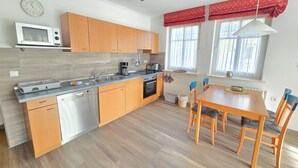 A modern kitchen with wooden cabinets, a microwave, a sink, and a dining area with a table and chairs. - Comfort apartment with 1 bedroom and balcony on the upper floor (Ostseebad Binz)