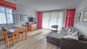 A modern living room with a wooden dining table, a grey sofa, and a TV on a wooden cabinet. - Comfort apartment with 1 bedroom and balcony on the upper floor (Ostseebad Binz)