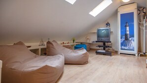 Un dormitorio estilo loft acogedor con techo inclinado, un televisor, un cartel de un faro y dos pufs.