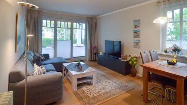 A modern living room with a sofa, coffee table, TV, and dining area. - Comfortplus vacation apartment with 1 bedroom and terrace on the first floor (Ostseebad Binz)