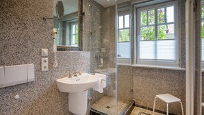 A modern bathroom with a granite countertop sink, a glass-enclosed shower, and a small white stool. - Comfortplus vacation apartment with 1 bedroom and terrace on the first floor (Ostseebad Binz)