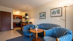 A living room with a sofa and chairs, a dining table, a kitchen in the background, and two framed pictures on the wall. - Comfort apartment with 1 bedroom and terrace on the first floor (Ostseebad Binz)