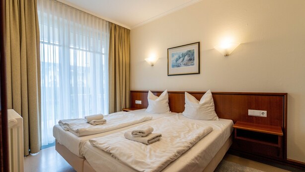 A hotel room with a large bed, two bedside tables, a nightstand, a framed picture on the wall, and a window with curtains. - Comfort apartment with 1 bedroom and terrace on the first floor (Ostseebad Binz)