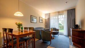 A modern living room with a dining area, featuring a wooden table, chairs, a sofa, and a TV. - Comfort apartment with 1 bedroom and terrace on the first floor (Ostseebad Binz)