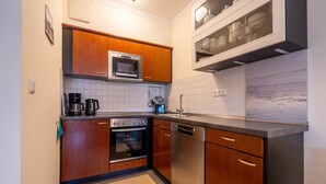 A compact kitchen with wooden cabinets, a microwave, a stove, and a dishwasher. - Comfort apartment with 1 bedroom and terrace on the first floor (Ostseebad Binz)
